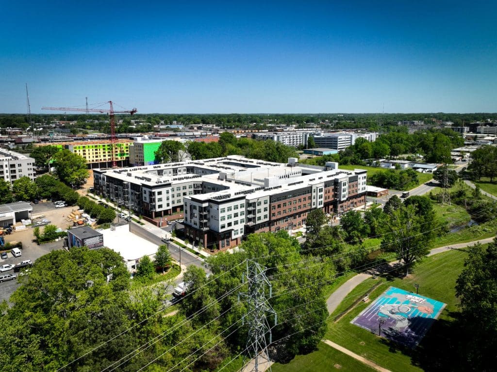 Aerial view of Alta Filament in Charlotte, a large apartment block surrounded by trees with the city beyond.