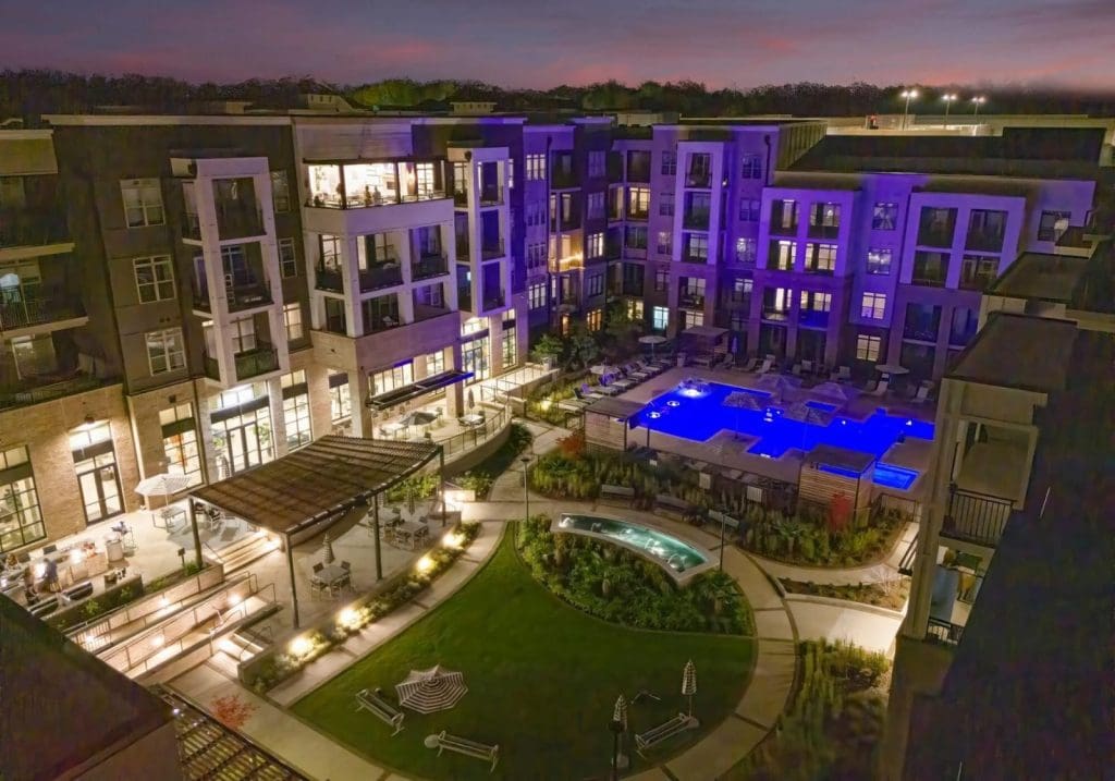 Providence Row in Charlotte photographed by drone at twilight, the lit apartment buildings wrapped around a courtyard and pool.